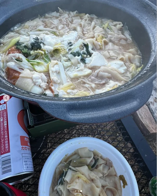 A pot of sliced ingredients and vegetables on a portable stove, with a serving bowl in front.