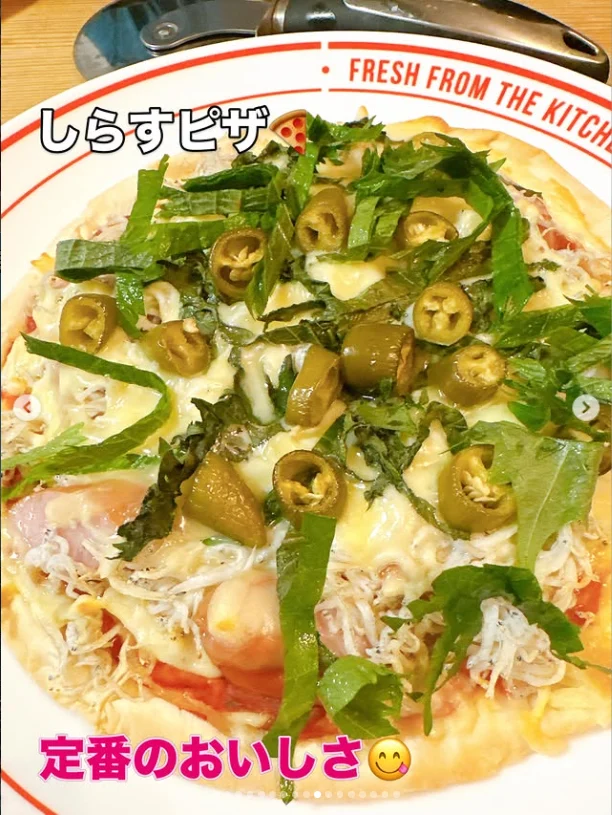 A pizza with green leaves, sliced green peppers and fine pale toppings, with Japanese text over the photograph.