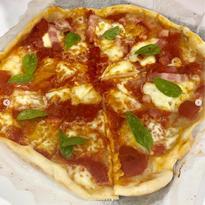 A pizza with red sauce, melted cheese and green leaves on a white plate.