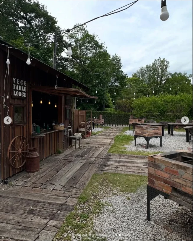 A wooden building and outdoor seating among trees beneath string lights.