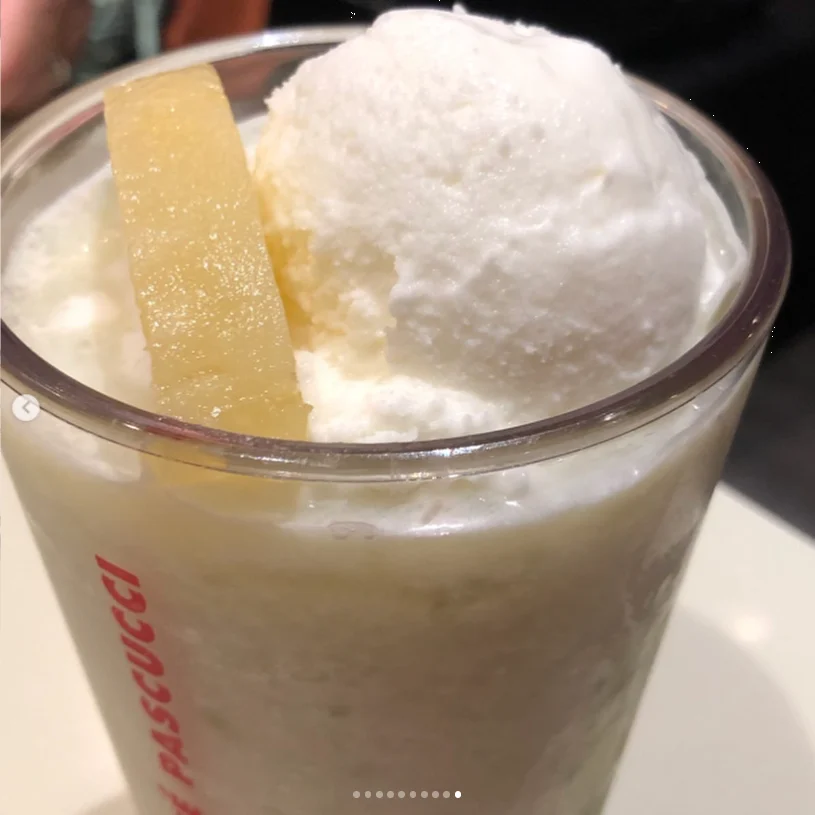 A tall glass containing a pale dessert drink topped with a white scoop and a wafer.