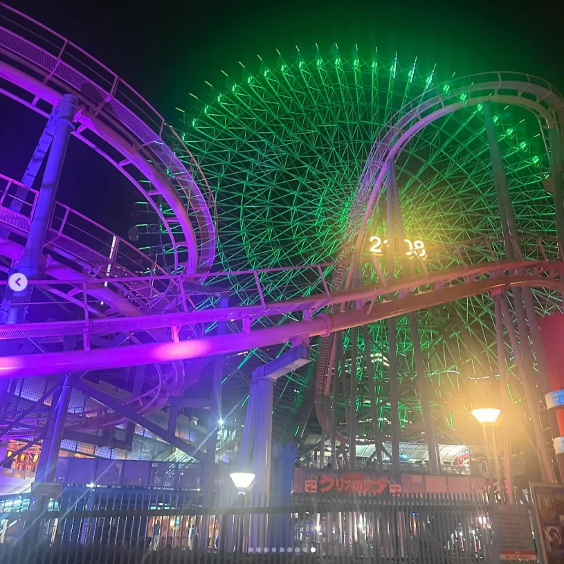 A Ferris wheel and roller-coaster tracks illuminated in green and purple at night.