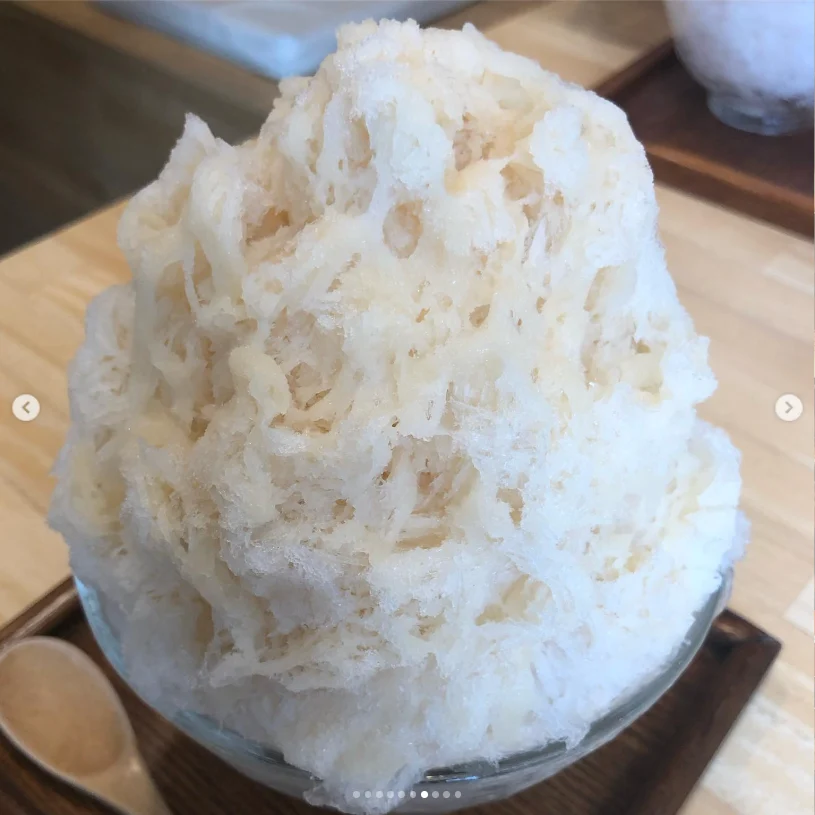 A tall mound of white shaved ice with a pale topping.
