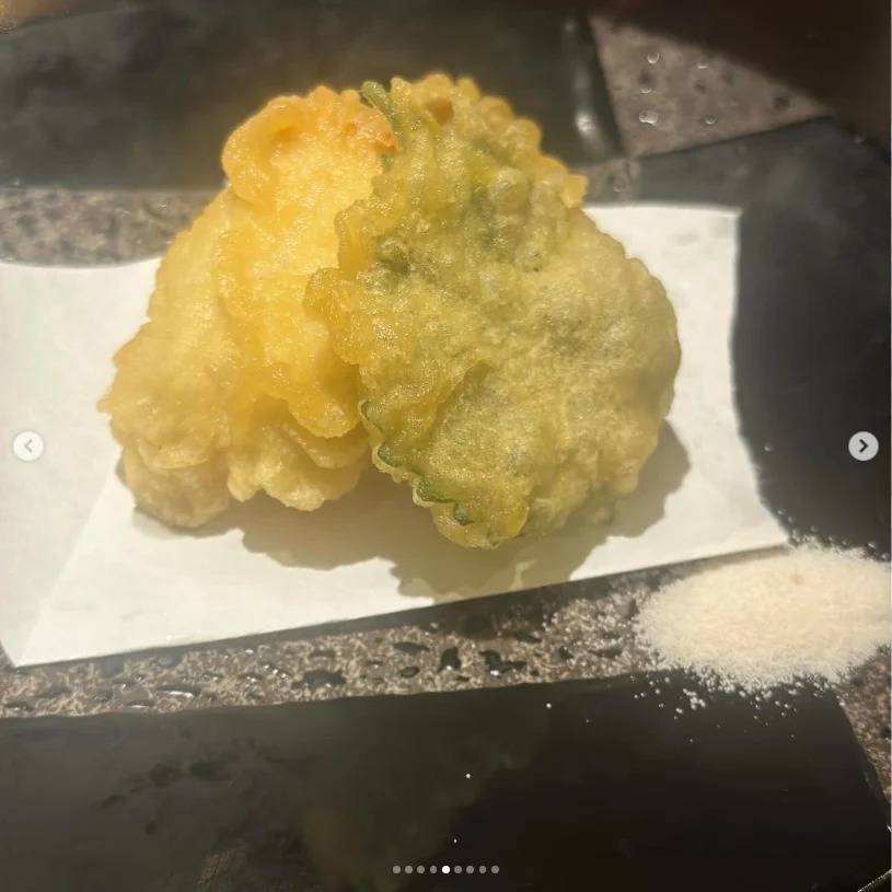 Two golden battered pieces on a black plate beside small piles of salt.
