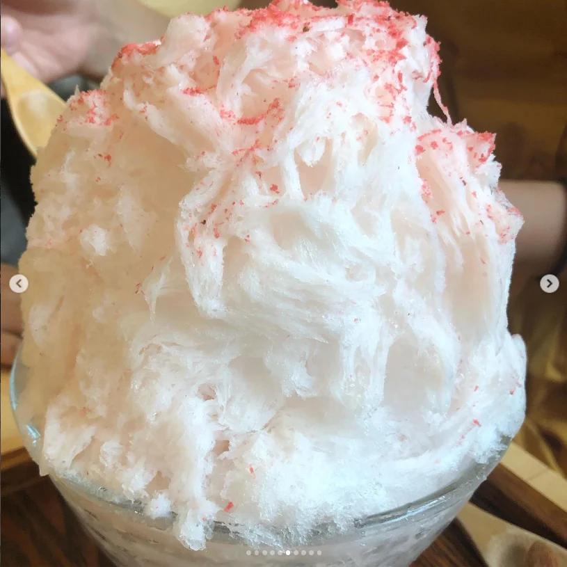 A mound of white shaved ice with a pink topping.