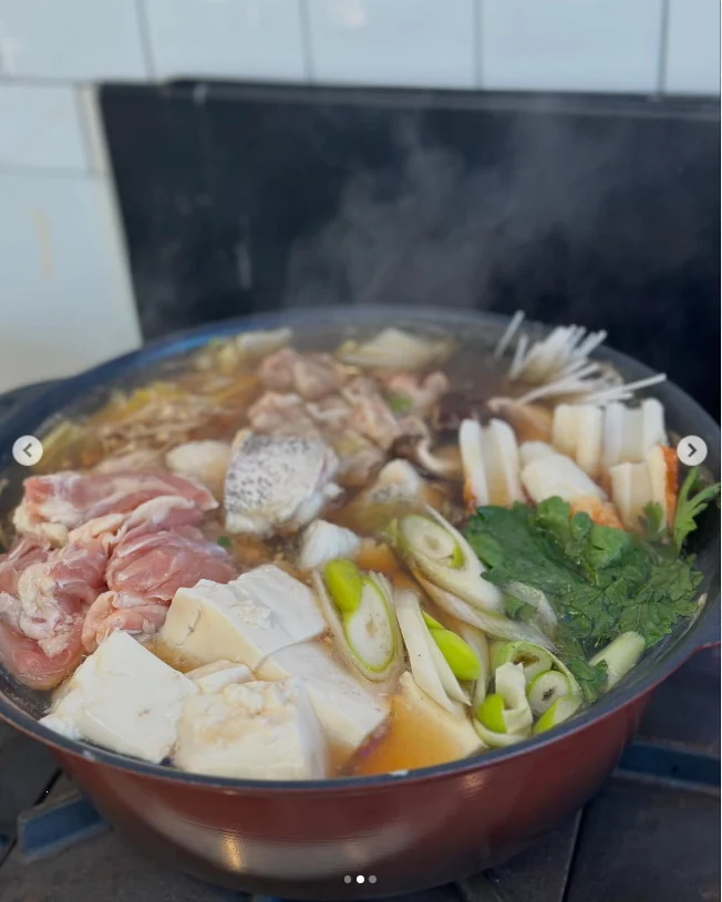 A steaming hot pot filled with sliced meat, pale blocks and assorted vegetables.