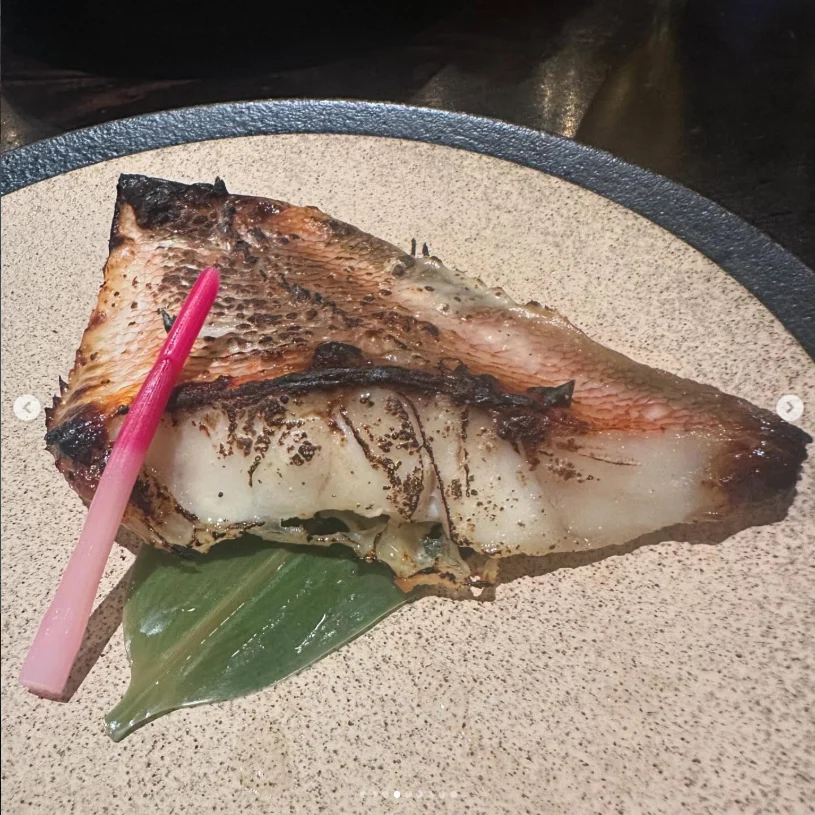 A browned fish fillet on a green leaf with a slender pink garnish.