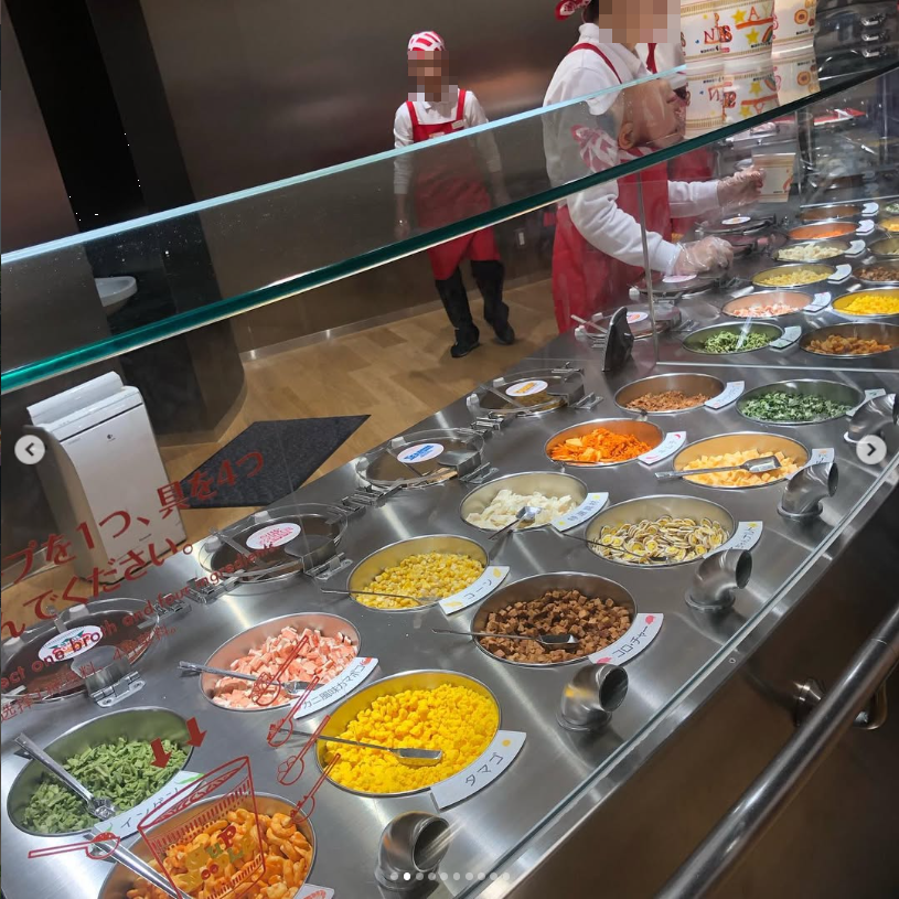 A glass-covered counter of colourful ingredients with a worker behind it.