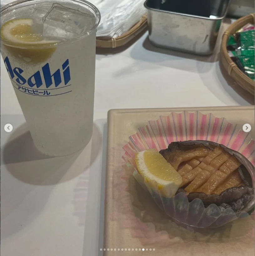 A tall iced drink beside sliced shellfish in its shell with a lemon wedge.