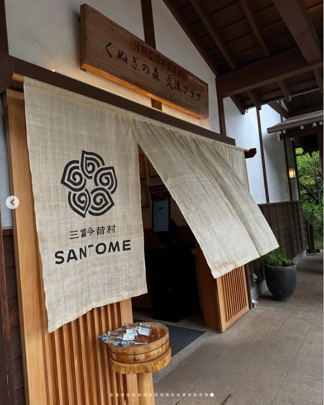 A wooden doorway with a white split curtain bearing a circular logo and Latin lettering.