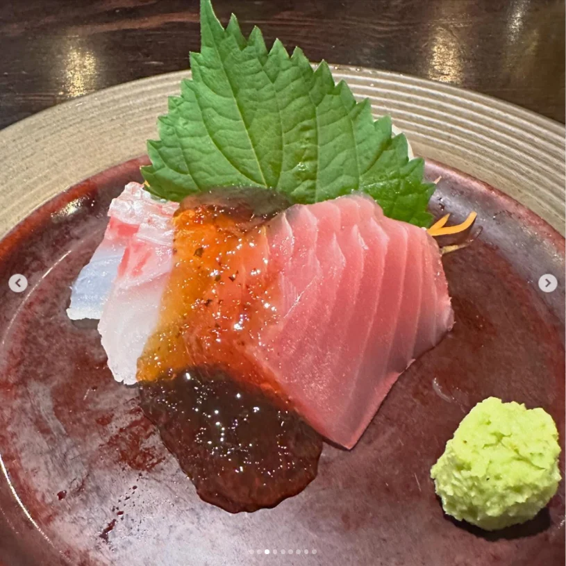 Pink and white slices on a dark plate with small orange beads, a green leaf and green garnish.