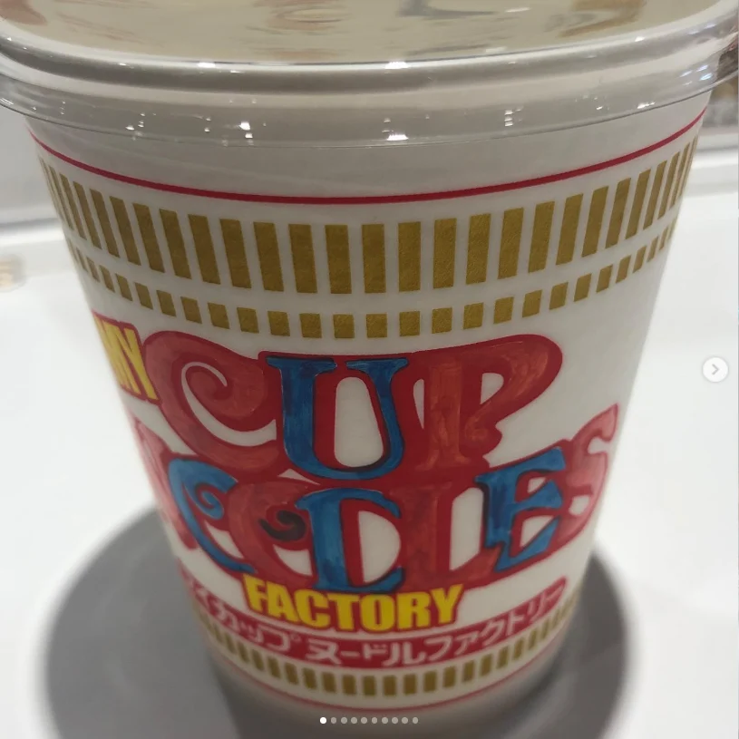 A lidded cup with colourful Cup Noodles Factory lettering shown close up.