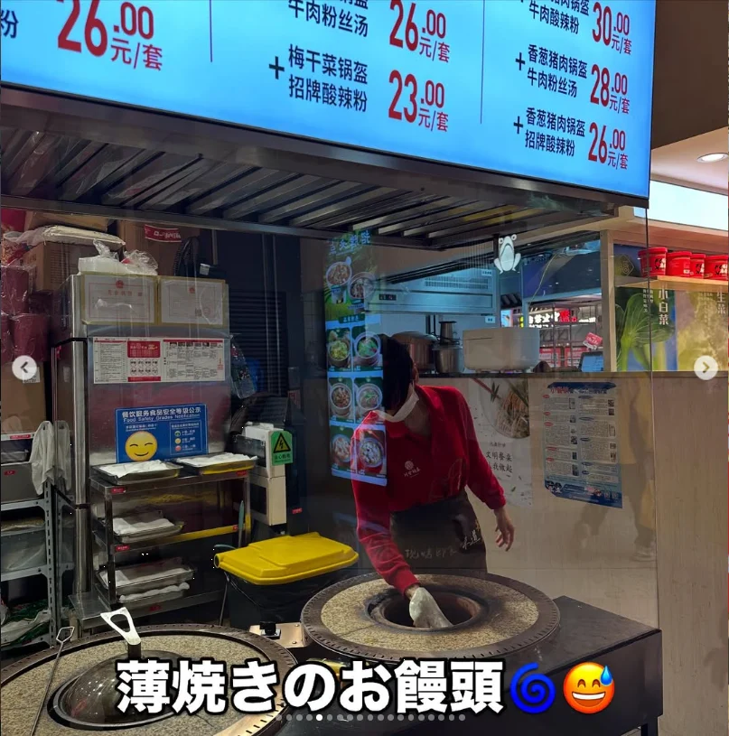 A food-stall worker cooking at a round griddle below menu boards.