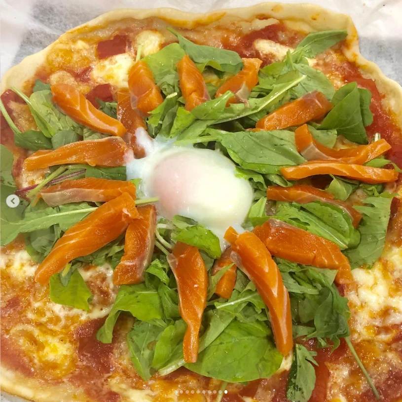 A pizza topped with green leaves, orange slices and a rounded white topping in the centre.