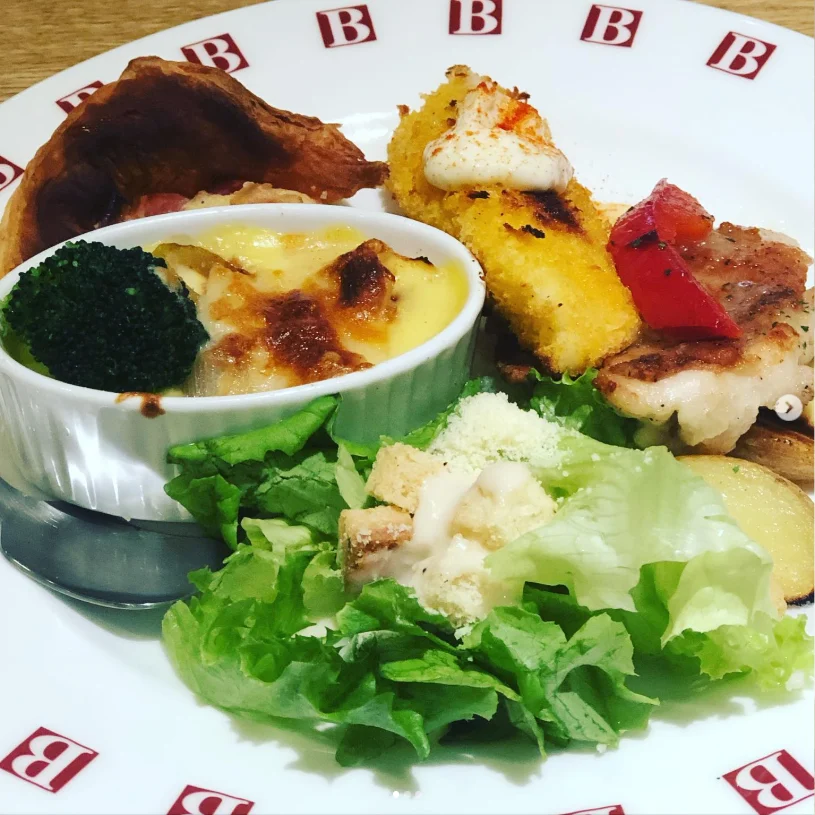 A plate of salad and assorted dishes beside a small ramekin of browned baked food.