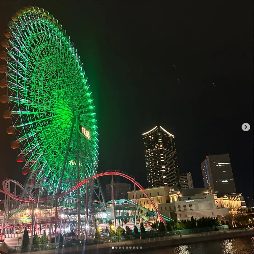 A green-lit Ferris wheel beside buildings and water at night.