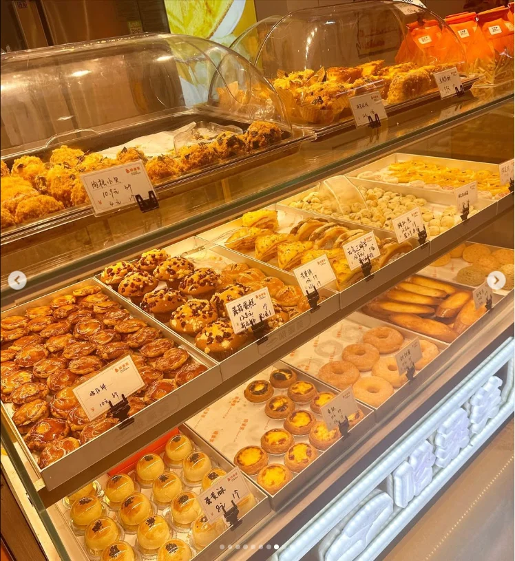A glass-fronted counter with rows of small food displays and Japanese labels.