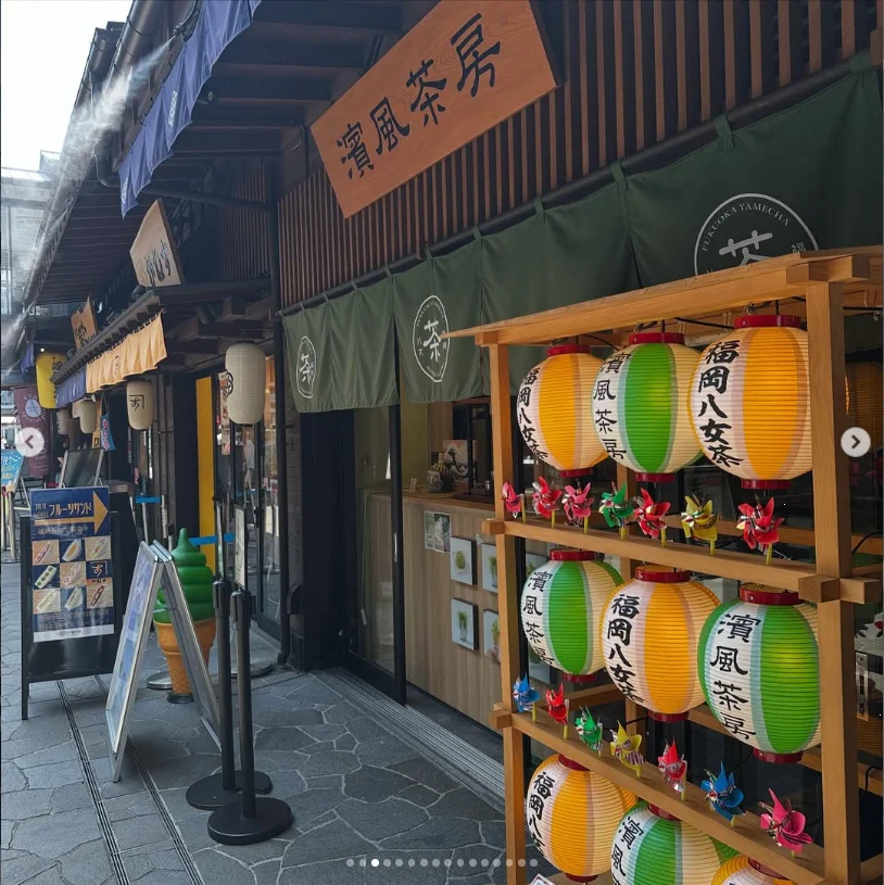 A wooden storefront with hanging green curtains and a rack of small barrel-shaped decorations.