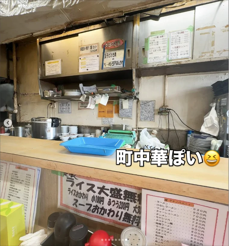 A small counter kitchen with pots, wall menus and notices, with Japanese text over the photograph.