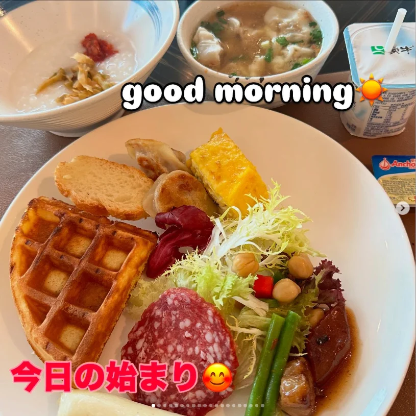 A breakfast plate with a waffle, egg, sliced sausage and salad beside small bowls and a drink.