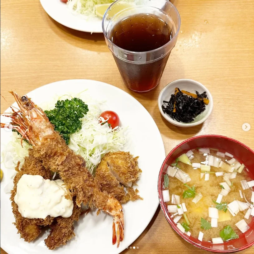 A tray meal with breaded pieces and prawns, salad, rice, soup and a glass of tea.