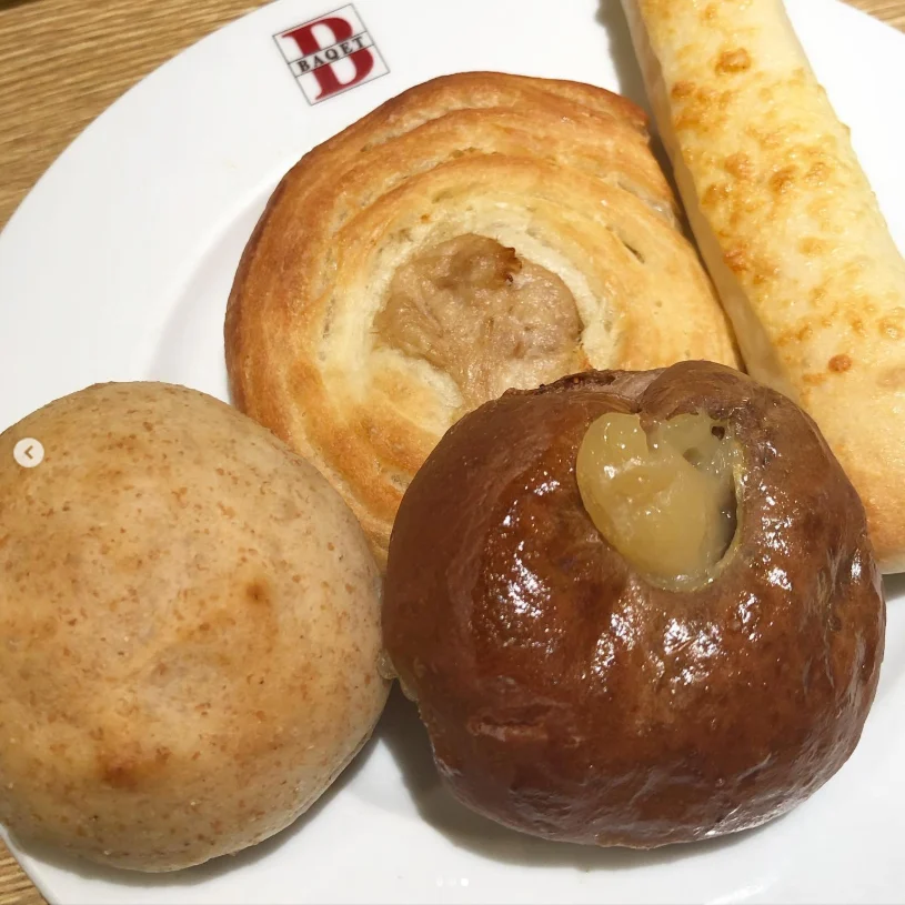 Four pieces of bread on a white plate, including a swirled roll and a long breadstick.