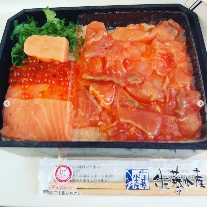 An open bento with orange slices, small orange beads and green garnish, with wrapped chopsticks below.