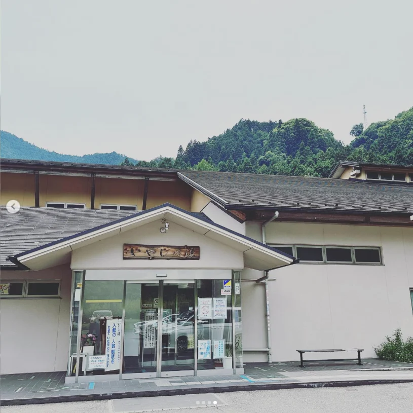 A pale building with a central entrance and Japanese signs, with wooded hills behind it.