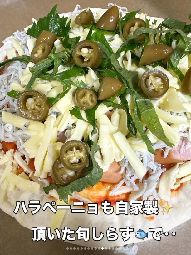 A pizza with green leaves, sliced green peppers and fine pale toppings, with Japanese text over the photograph.