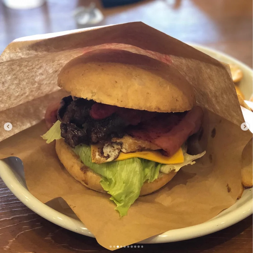 A burger with lettuce, cheese and a dark filling partly wrapped in brown paper.